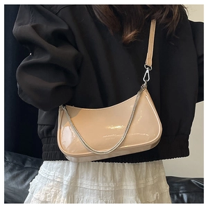 Close-up of beige patent leather hobo bag with silver chain detail and sleek moon shape