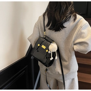 Detail of black faux leather crossbody bag with woven texture, gold hardware and white pompom