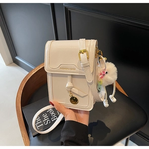 Détail du sac à bandoulière en cuir blanc cassé avec pendentif doré et pompon en fourrure