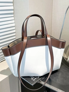 Large minimalist tote bag in white and brown leather with dual straps on dark tabletop