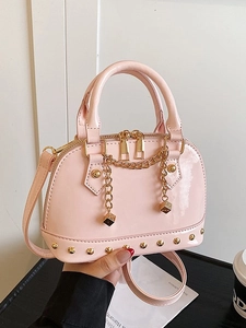 Pink patent leather shell bag with gold rivet accents and chain strap in hand