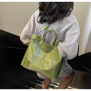 Detail of green glossy tote bag featuring white TOTE BAG text and metallic shoulder strap
