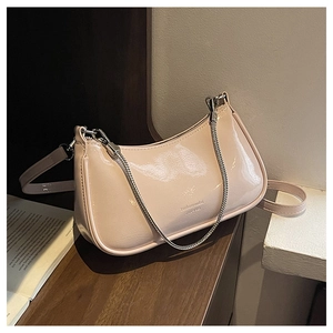 Detail of cream patent leather baguette bag with silver chain and dual straps on wooden desk