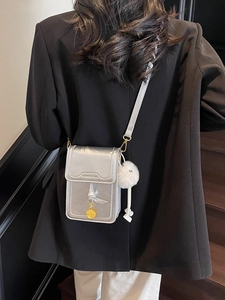 Sac à bandoulière argenté métallisé avec détails dorés et pompon porté par un mannequin