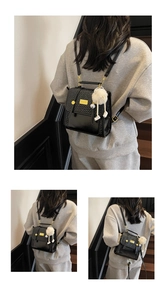 Detail of black leather backpack featuring woven texture flap and white fur ball pendant