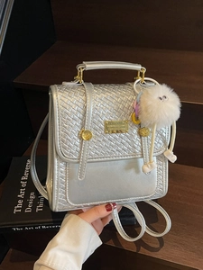 Silver woven handbag and backpack with plush charm and metal logo on wood background