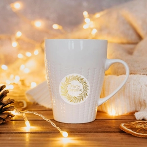 Close-up of white ceramic mug with knit texture and gold Merry Christmas wreath decal
