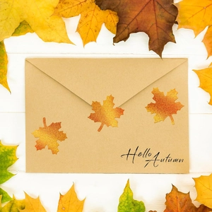 Holographic maple leaf stickers on a brown envelope with Hello Autumn text on white wood