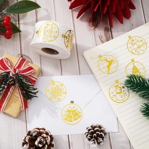 Gold foil Christmas stickers roll with reindeer and snowman designs on white wood background