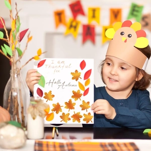 Girl wearing turkey headband and autumn leaf stickers with festive greeting card detail