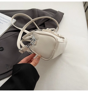 Detail of a creamy white PU leather crossbody bag with silver zipper and bow drawstring