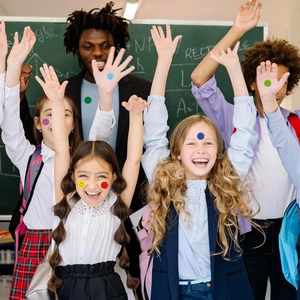 Close-up of children in a classroom wearing colorful round happy smile reward stickers