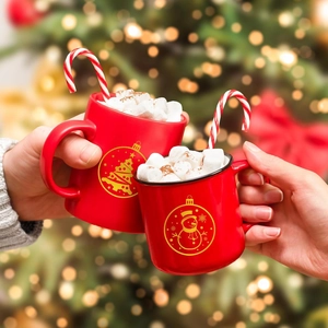 Detail of red Christmas mugs with gold foil snowman and tree designs in a festive setting