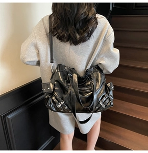 Model wearing a black glossy punk tote bag with silver rivets and buckle details