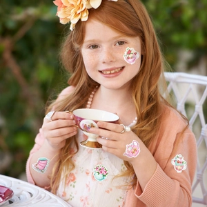 Floral tea party theme stickers on a girl's arm and face in an outdoor garden scene