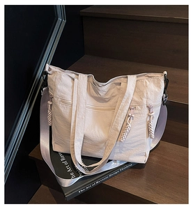 Detail of off-white ruched nylon tote bag with braided zipper pull on wooden steps