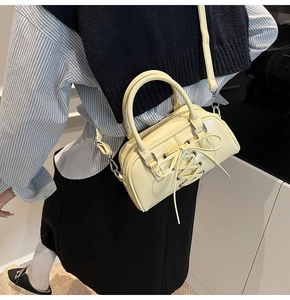 Detail of pale yellow crossbody bag with glossy finish and ribbon bow decoration
