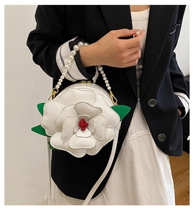Detail of 3D white flower crossbody bag with pearl handle and green leaf accents