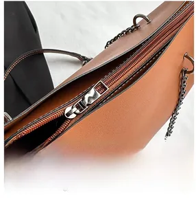 Close-up of silver metal zipper and chain links on a brown leather tote bag