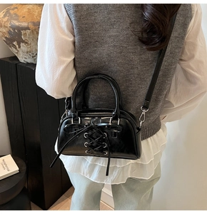 Close-up of black glossy crossbody bag featuring a decorative ribbon bow detail