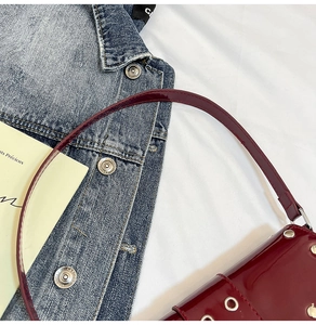 Détail du sac à bandoulière en cuir verni rouge foncé avec œillets argentés et lanière
