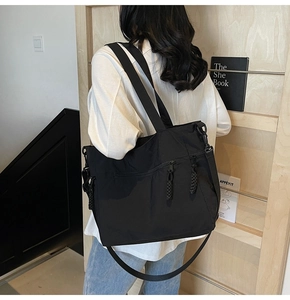 Detailed side view of the black tote bag with braided zipper pulls shown on a model