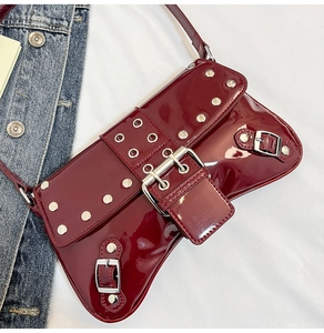 Détail d'un sac d'épaule bordeaux en cuir verni avec rivets argentés et boucles