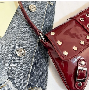 Détail du sac à épaule en cuir verni bordeaux avec rivets argentés sur fond denim