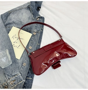 Vue détaillée du sac à bandoulière en cuir verni rouge foncé avec base incurvée