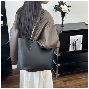 Detail of a large black leather tote bag featuring a stylish silver chain and leather strap