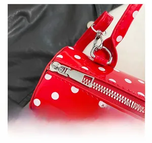 Détail de la fermeture éclair argentée sur le sac à bandoulière rouge à pois verni