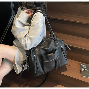 Close-up of black pebbled leather tote bag with silver zippers on wooden stairs