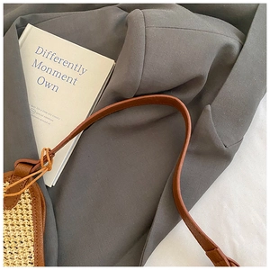 Detail of straw tote bag with brown leather trim and shoulder straps on grey blazer