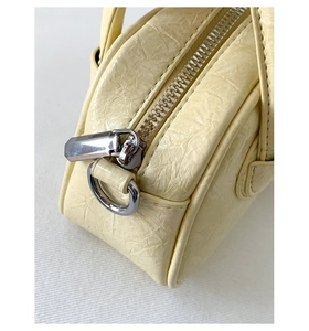Detailaufnahme des Reißverschlusses und der silbernen Beschläge der cremefarbenen Tasche