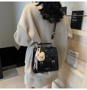 Detail of a black printed PU leather backpack featuring metal buckles and a plush bear charm