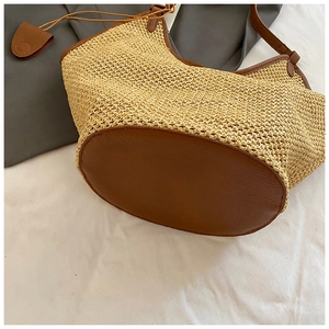 Macro view of woven straw beach bag featuring brown leather base and side pendant detail