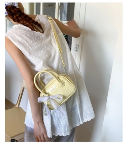 Gelbe Mini-Bowlingtasche aus Leder mit Spitzenschleife und Perlenanhänger am Modell
