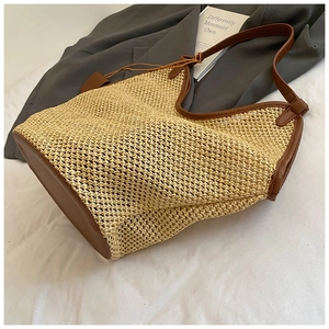 Detail of woven straw tote bag with brown leather handles on a minimalist background