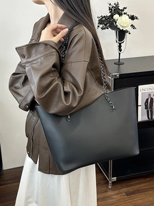 Minimalist black leather tote bag with stylish metal chain strap shown on a model