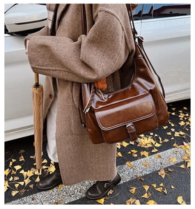 Close-up of a vintage dark brown oil wax leather shoulder bag with buckle pocket detail