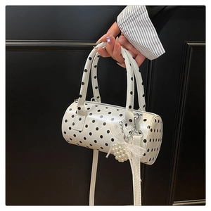 Detailed view of polka dot cylinder bag with pearl bow charm and glossy leather finish