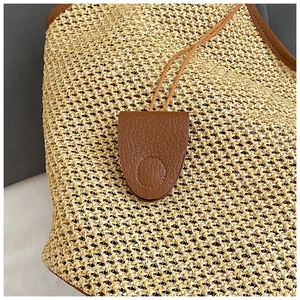 Close-up of woven straw bag detail featuring brown leather magnetic closure and texture