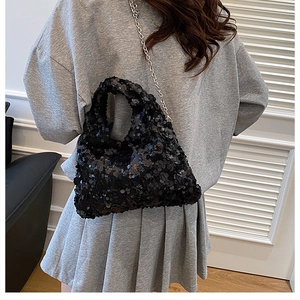 Detail of black sequined handbag featuring a silver chain strap worn by a model