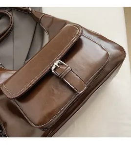 Detail of dark brown wax leather shoulder bag with silver buckle and white stitching