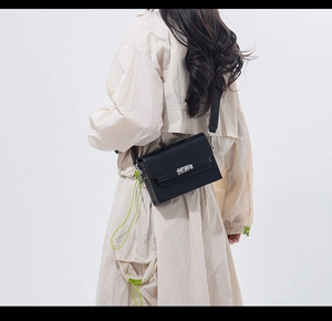 Close-up of black leather shoulder bag with silver clasp and neon green charm detail