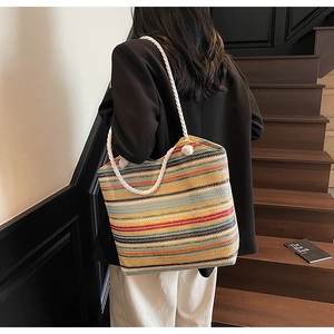Rainbow striped woven tote bag with white rope straps and pom-pom detail on shoulder