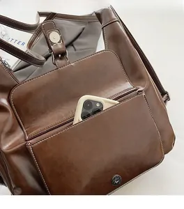 Detail of dark brown wax leather bag front pocket with magnetic closure holding a smartphone
