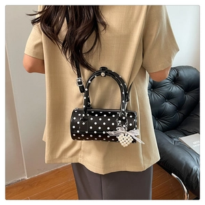 Close-up of cylindrical polka dot bag with glossy finish and pearl bow charm detail