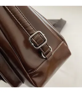Close-up of dark brown oil wax leather bag with silver hardware and white stitching