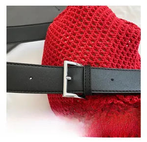 Detail of adjustable black leather strap and silver buckle on a red woven tote bag